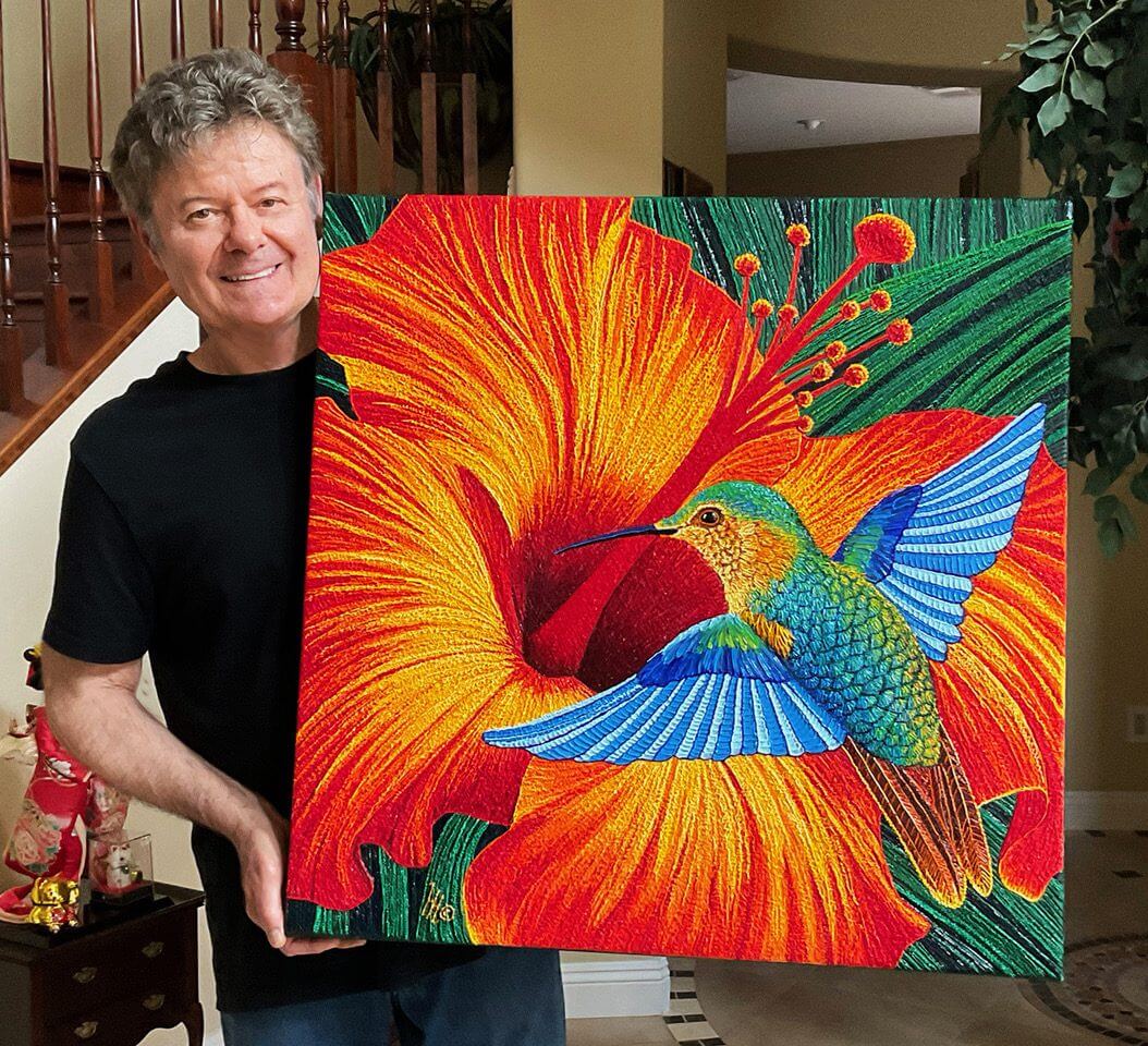 Man holding vibrant hummingbird and flower painting.